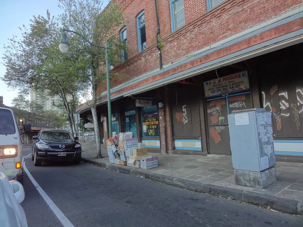 A produce wholesaler and other small storefronts on a street in Honolulu's Chinatown