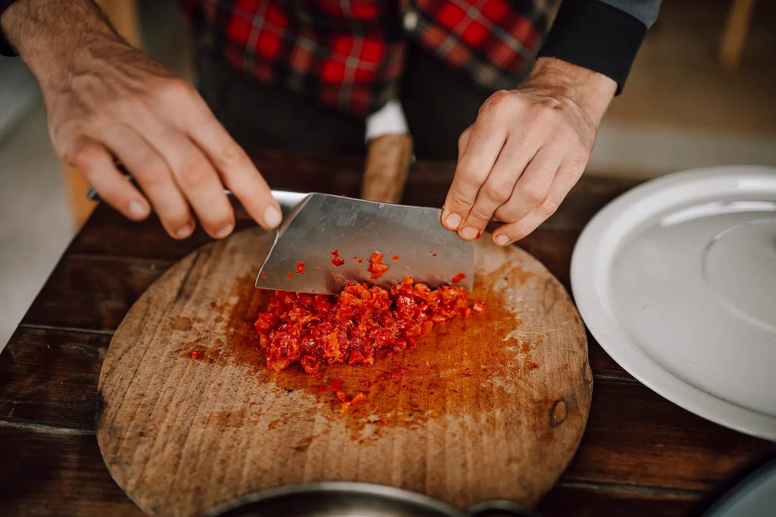 Cook chopping red peppers with a cleaver on a round wooden cutting board