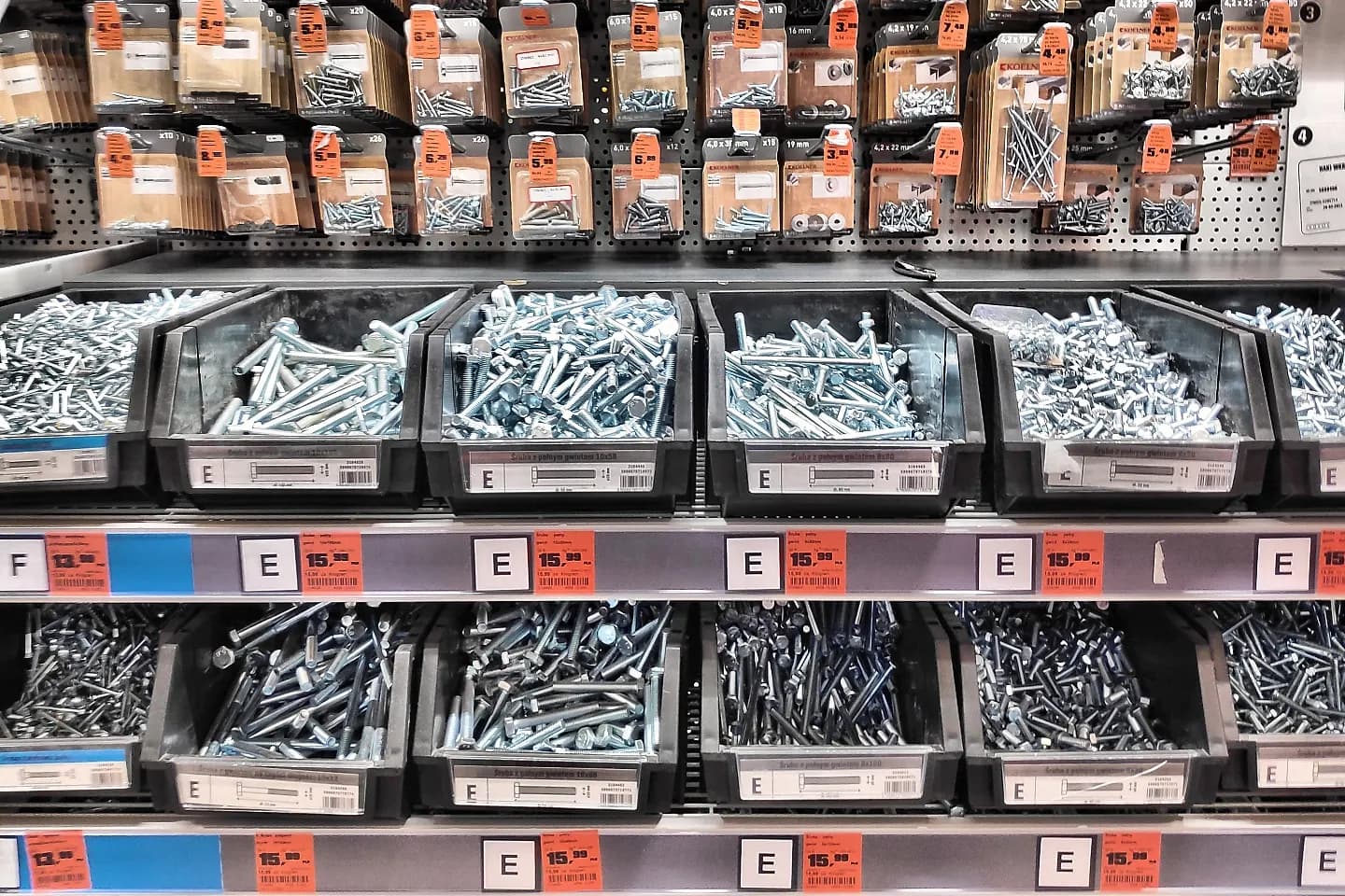 Bins of bolts and boxed screws in a hardware store, each with an orange shelf price label