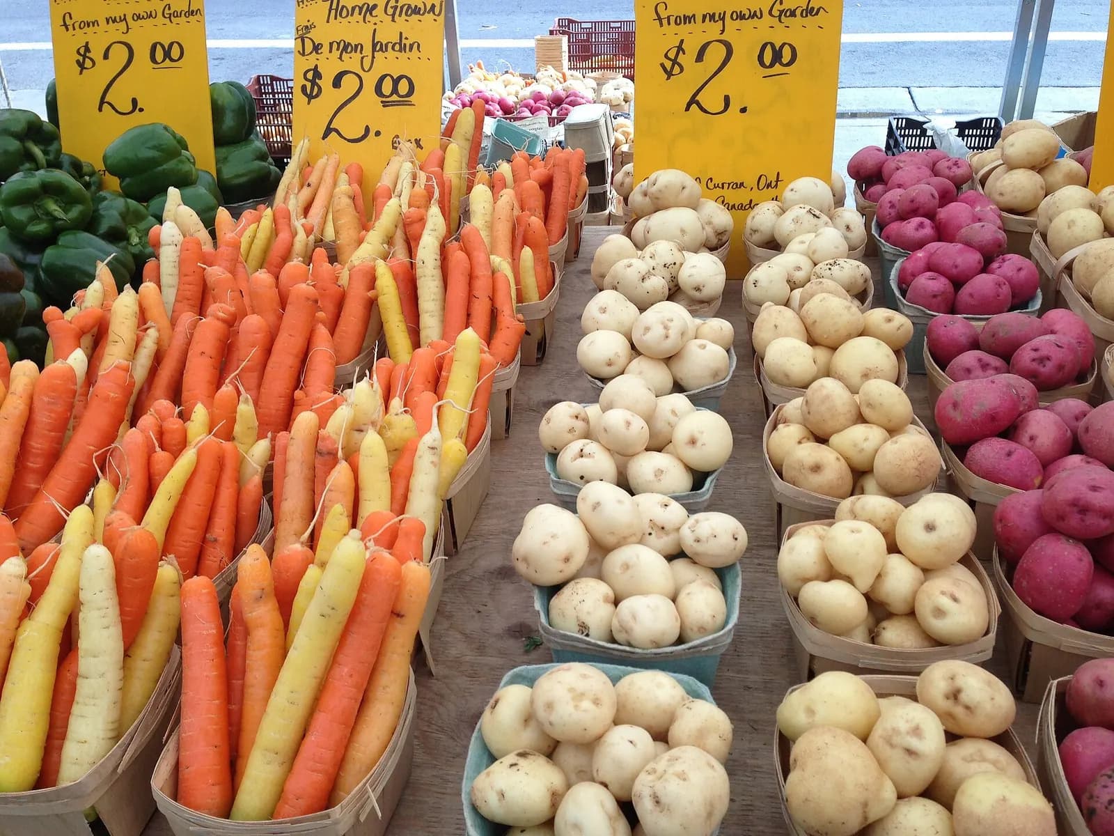 Farm stand with crates of carrots, potatoes and red potatoes under handwritten $2.00 price signs