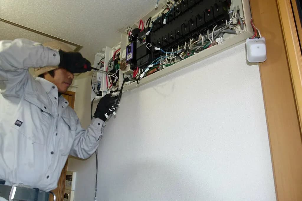 Electrician in gloves wiring a breaker into an open electrical panel on a wall