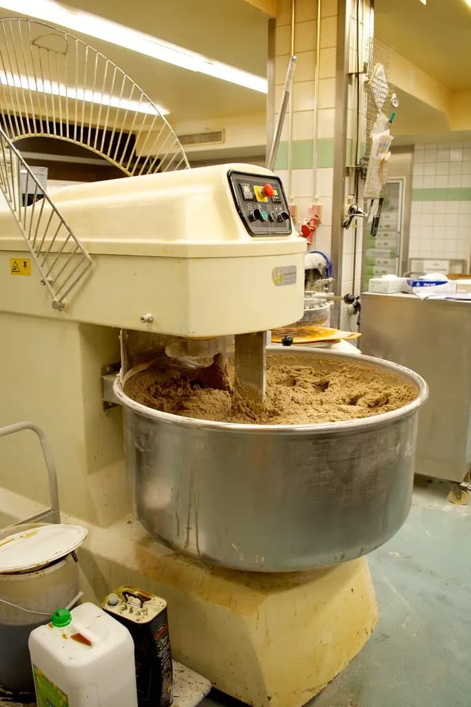 A large commercial spiral mixer kneading dough in a stainless steel bowl in a bakery production room