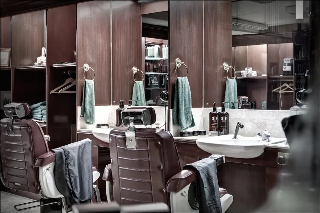 Two leather barber chairs facing mirrored stations with wash basins, towels and product shelves