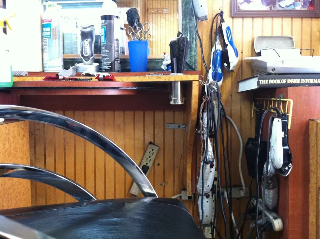Corded hair clippers and trimmers hanging beside a barber station with a jar of combs and disinfectant products