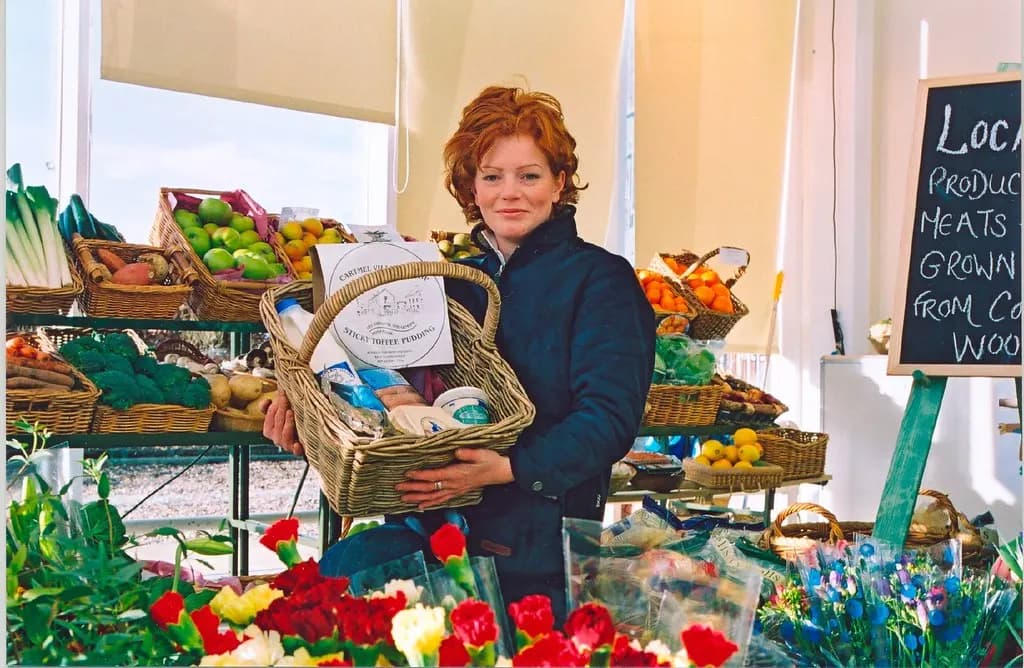 Owner of a small local produce shop holding a gift basket among crates of fruit, vegetables and flowers
