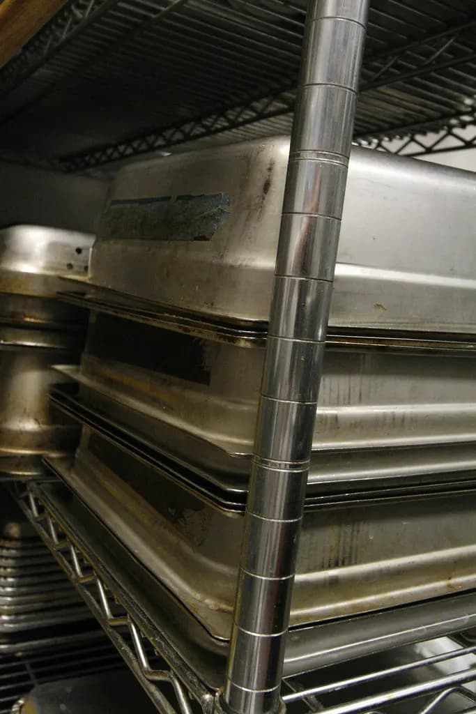 Stacks of stainless steel hotel pans on a wire shelf in a commercial kitchen