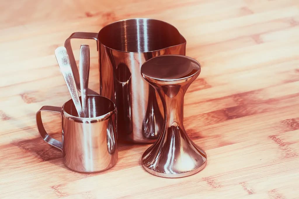 Stainless steel milk pitchers, a small espresso pitcher and a tamper on a wooden counter