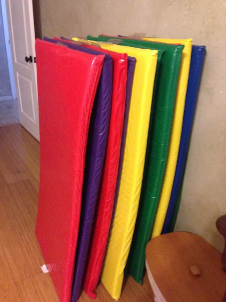 A stack of colourful vinyl nap mats leaning against a wall in a home child care room