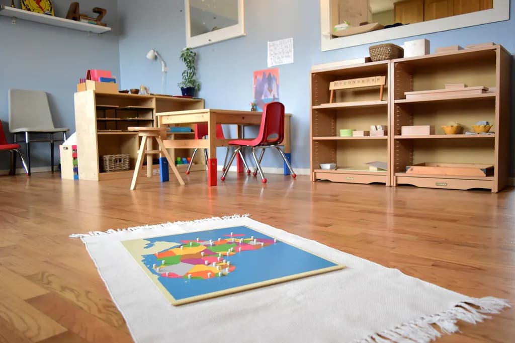 A bright preschool classroom with low wooden shelves, child-sized chairs and a learning mat on the floor