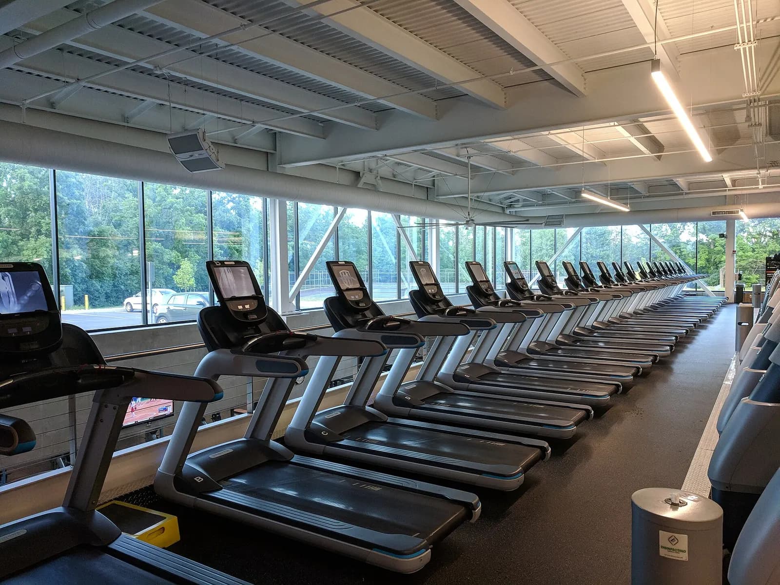 A long row of commercial treadmills facing floor-to-ceiling windows in a fitness center