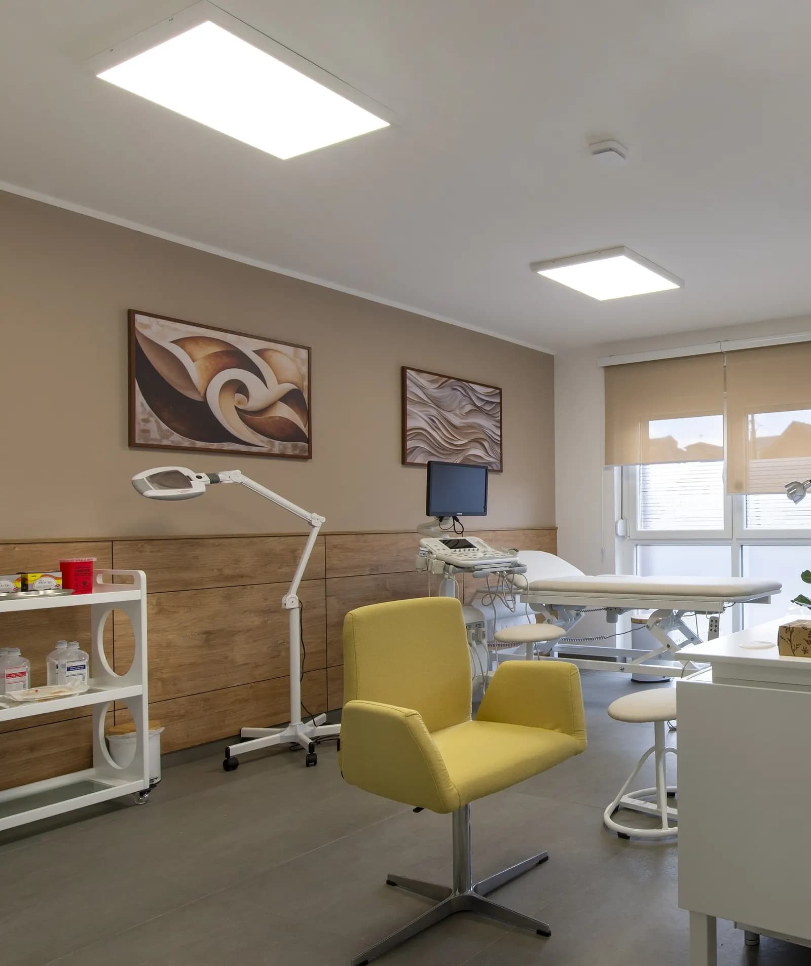 A small beauty treatment room with a treatment bed, magnifying lamp, supply trolley and client chair