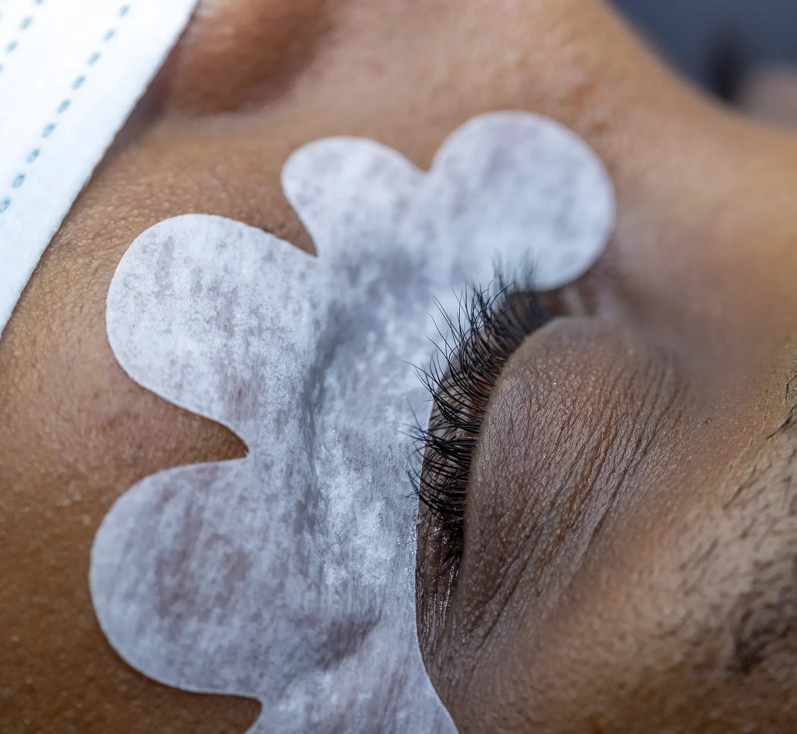 Close-up of a closed eye with a white under-eye gel pad taped below the lashes before an eyelash extension service