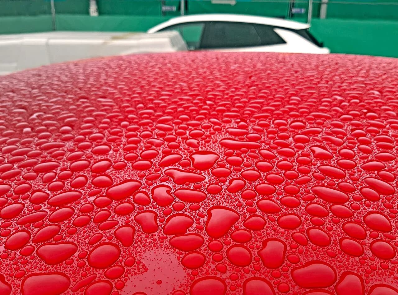 Water beading into round drops on a freshly polished red car roof