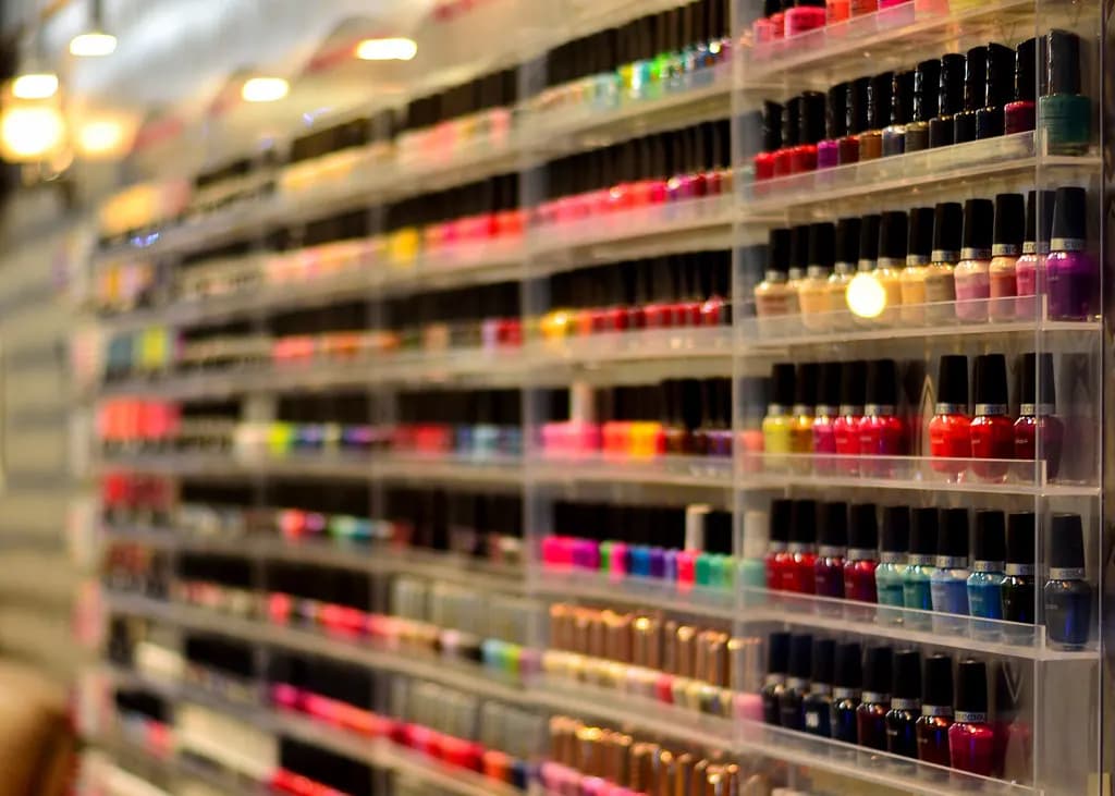 Rows of nail polish bottles in many colours on clear acrylic shelves along a salon wall