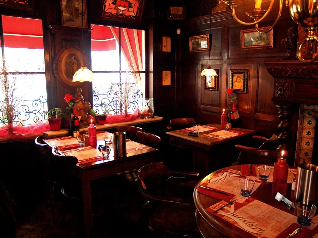A small restaurant dining room with set tables, candles and chairs by tall windows with red awnings