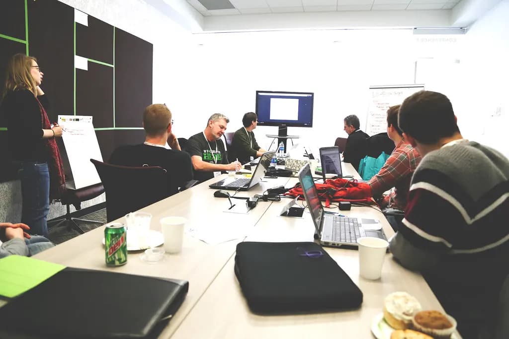 A facilitator leads a workshop for a small team seated around a conference table with laptops