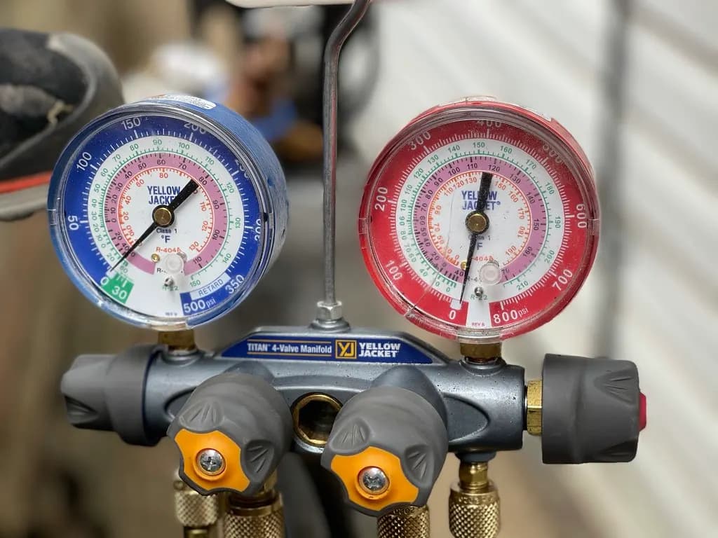 An HVAC manifold gauge set with blue low-side and red high-side gauges connected to a system