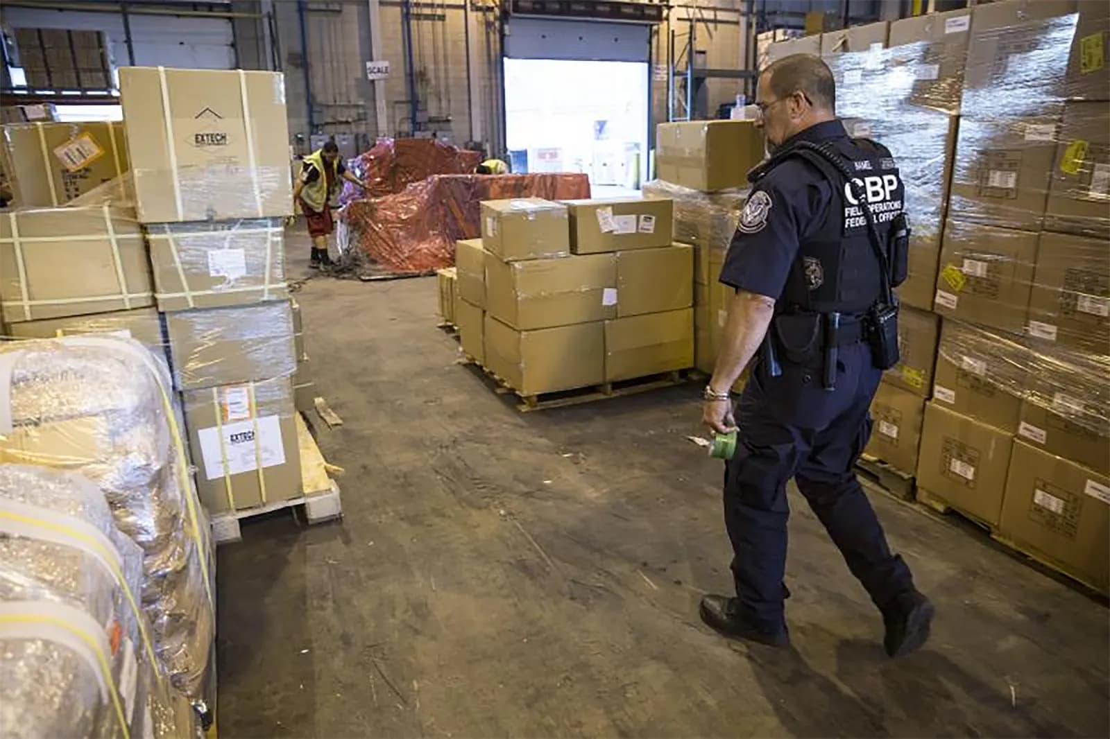 A US Customs and Border Protection officer walks past pallets of shrink-wrapped cartons in an import cargo warehouse