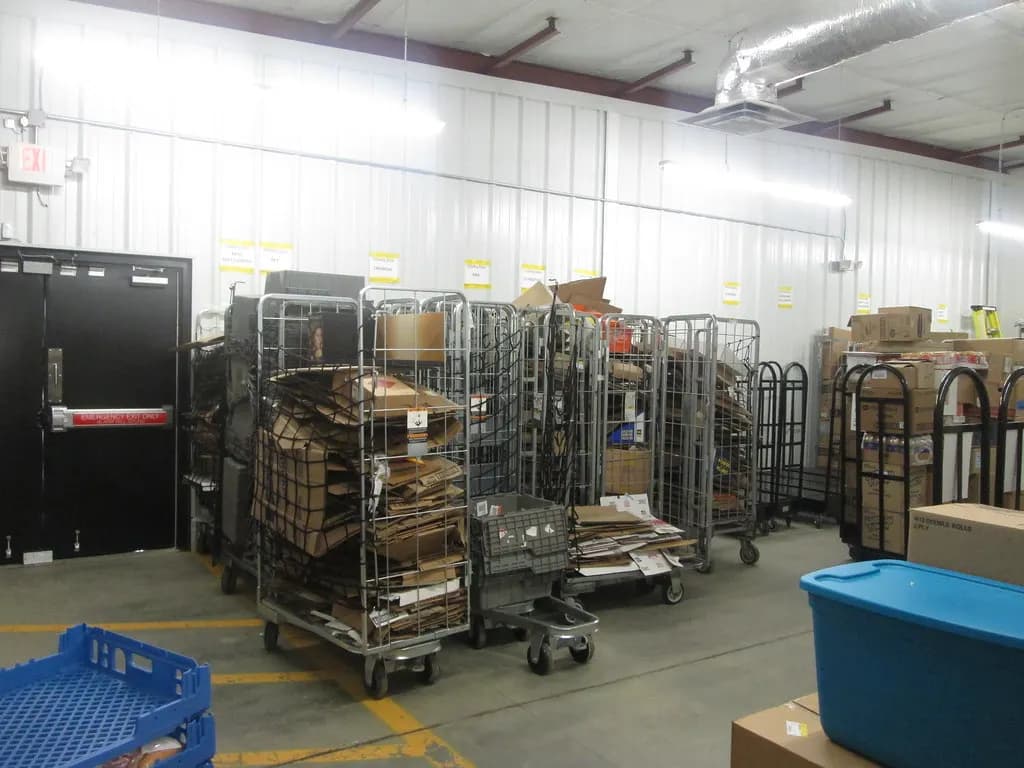 Store receiving area with roll cages of flattened cartons, stocking carts and a blue tote