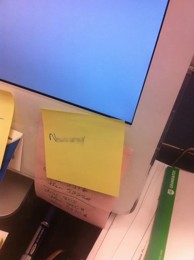 A yellow sticky note with a blurred password stuck to the bottom of a computer monitor