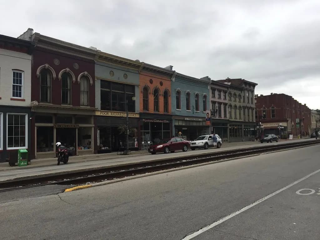Brick and painted storefronts along Broadway Street in downtown Frankfort, Kentucky, with rail tracks running down the street