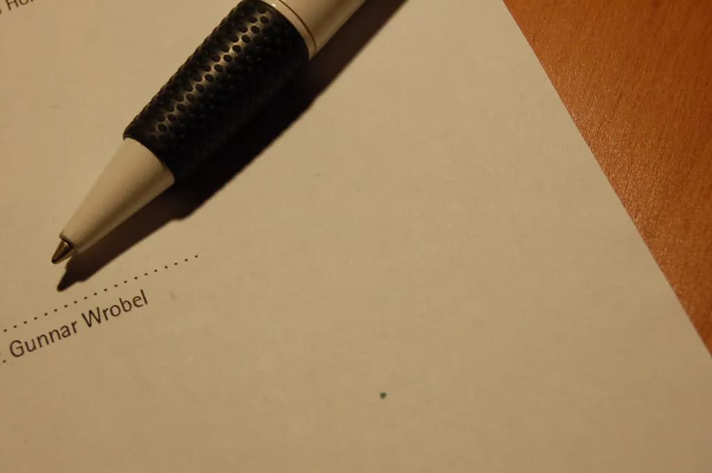 Ballpoint pen resting just above a dotted, still-unsigned signature line on a printed contract
