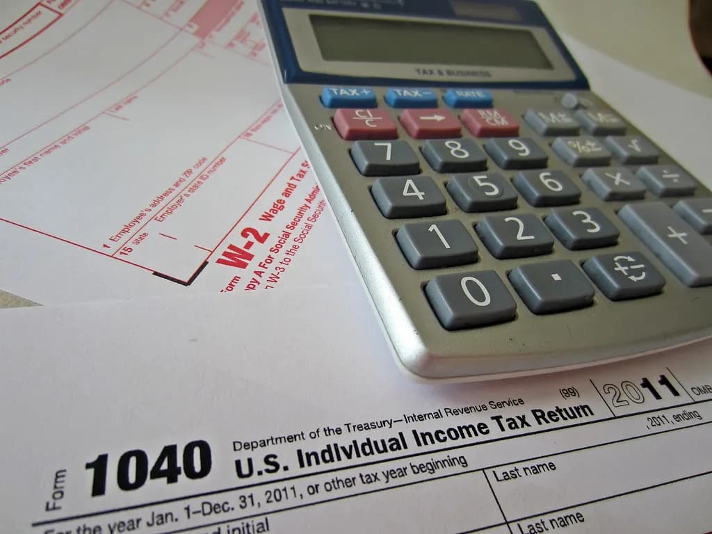 A Form W-2 and a Form 1040 individual tax return lying under a desk calculator