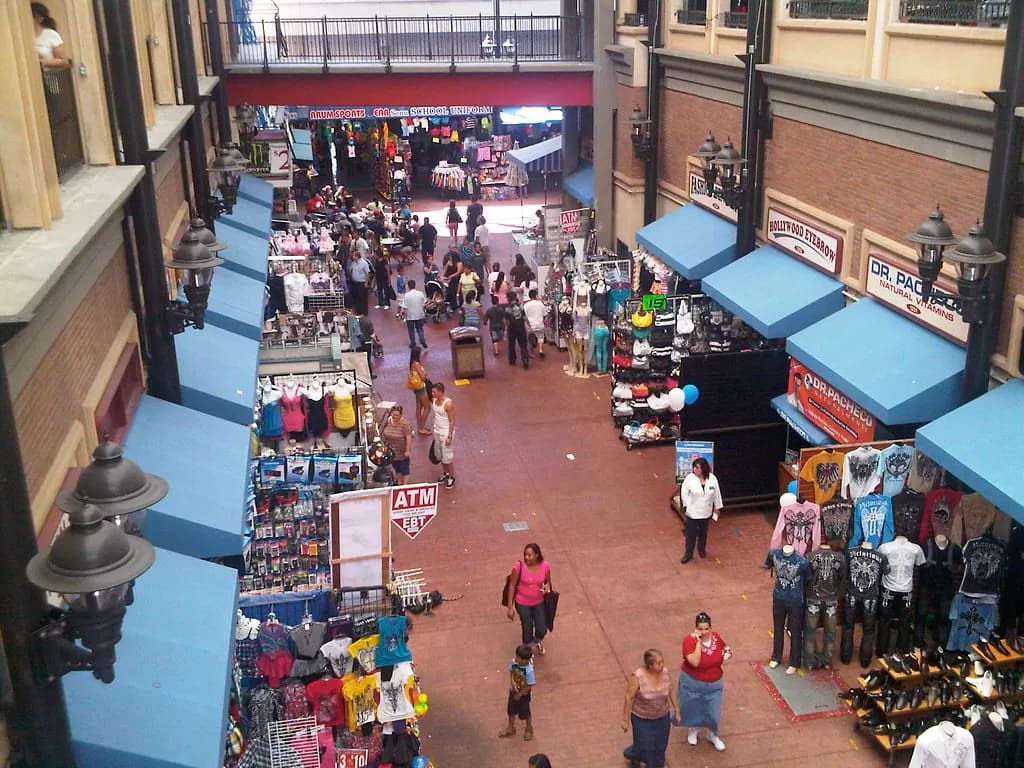 Small clothing and accessory shops under blue awnings in a pedestrian alley in the Los Angeles Fashion District