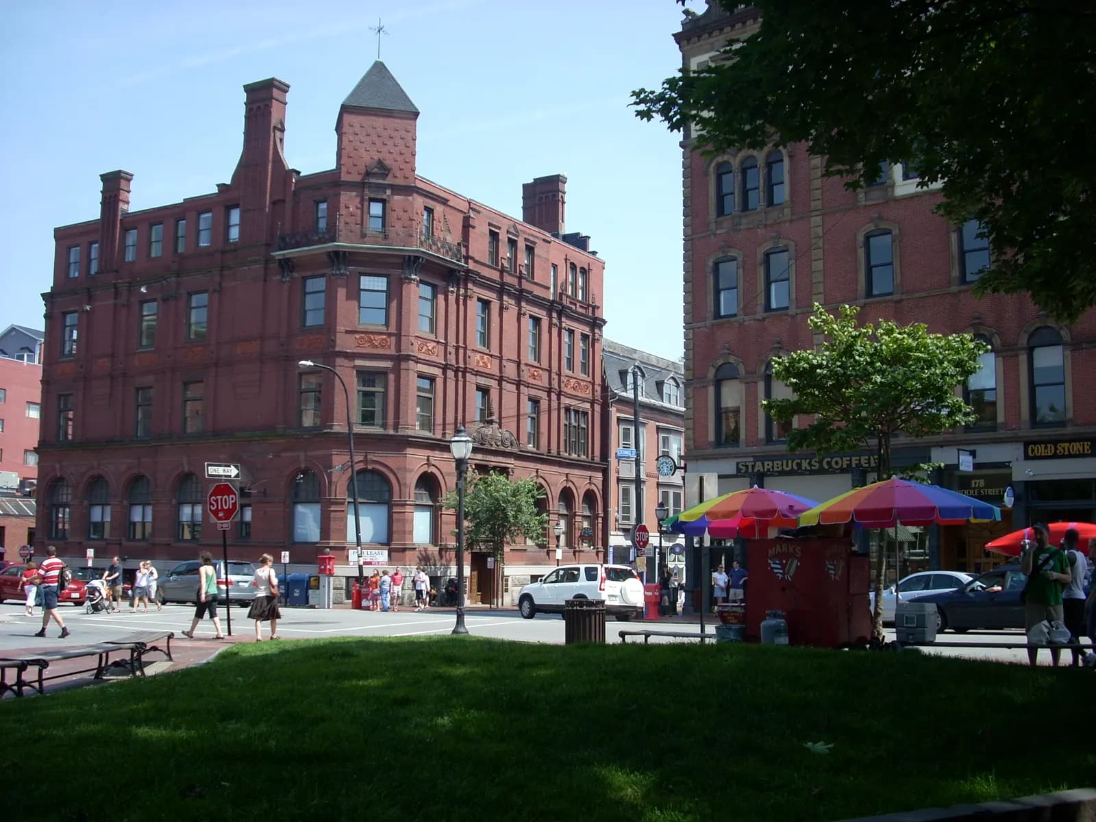 Food cart with colourful umbrellas at an Old Port intersection in Portland, Maine, in front of a red-brick building