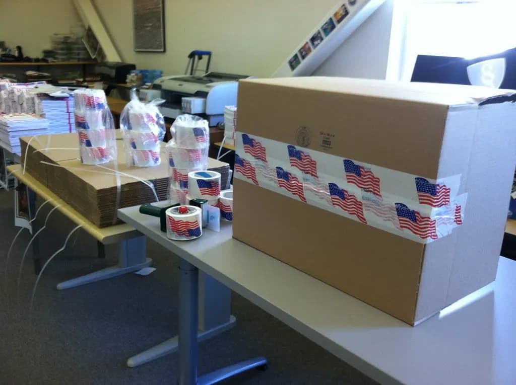 A sealed cardboard carton and rolls of packing tape on an office table set up for packing orders