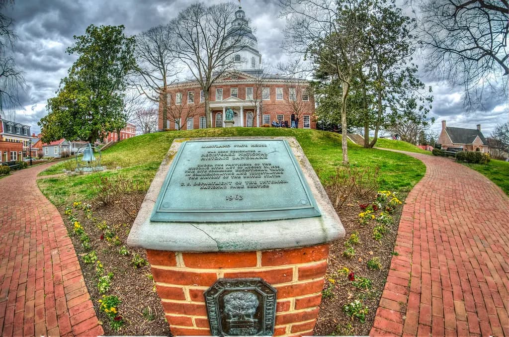 The red-brick Maryland State House in Annapolis with its white wooden dome, seen up a brick path past a bronze historic marker