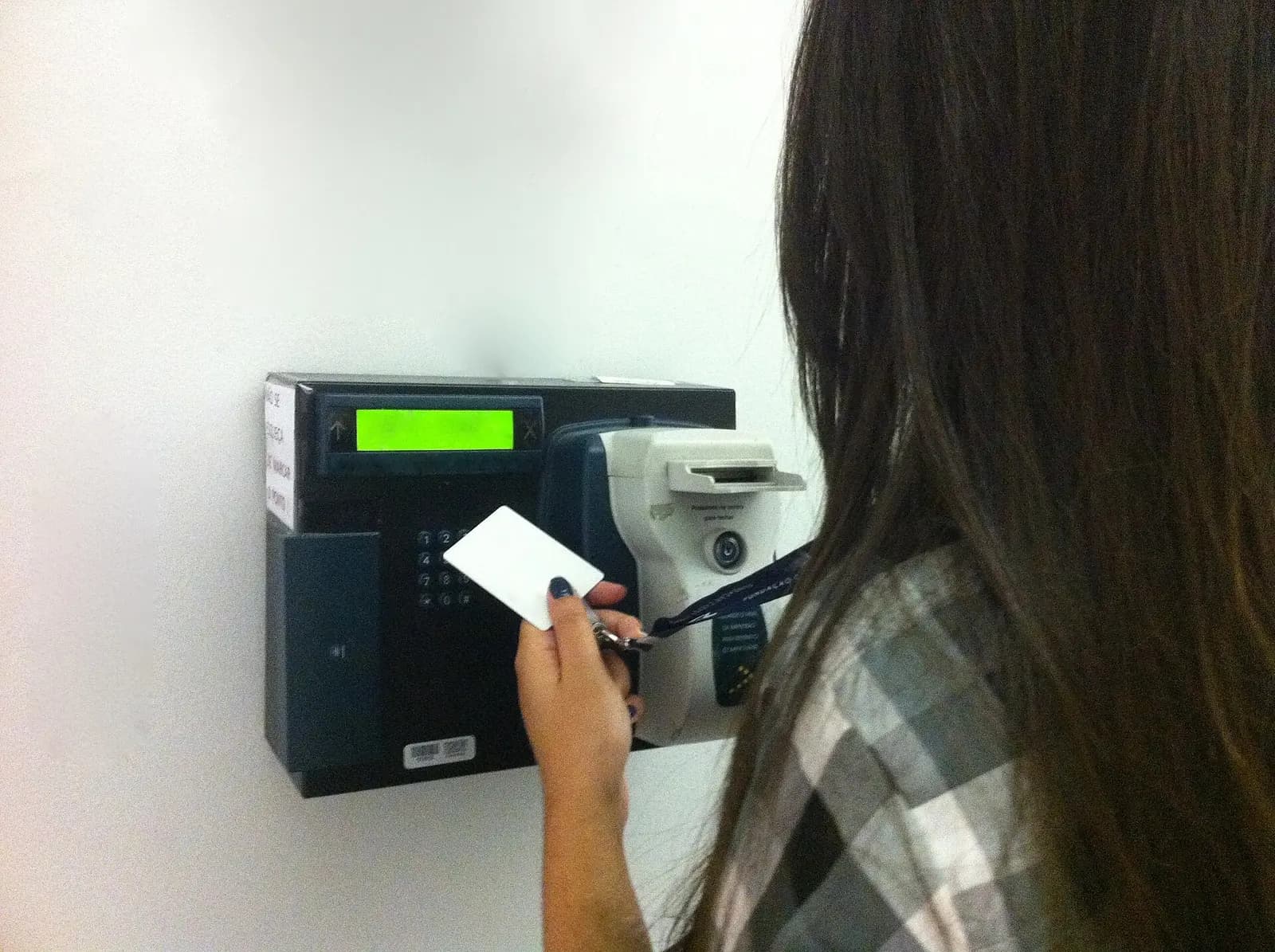 Employee holding a badge card up to a wall-mounted electronic time clock to record hours