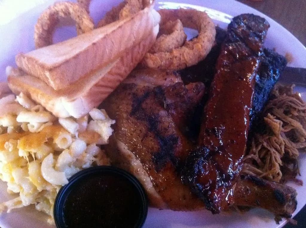 A barbecue platter with ribs, grilled chicken, pulled pork, mac and cheese and onion rings