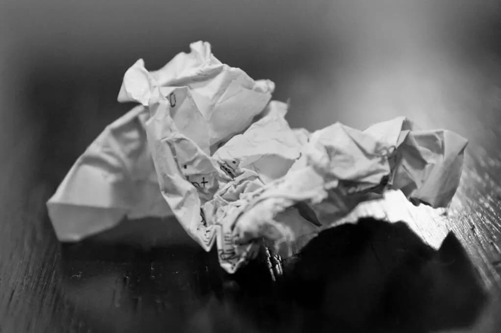 Black-and-white photo of a crumpled paper receipt lying on a wooden surface