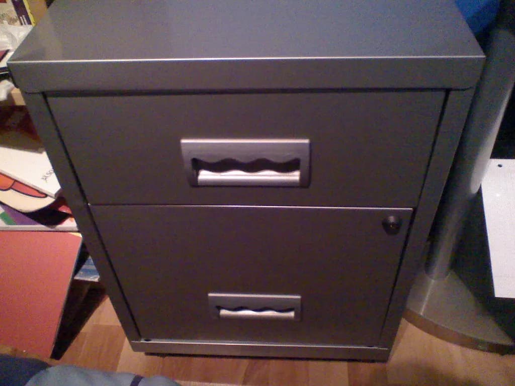 A grey two-drawer metal filing cabinet in a small office