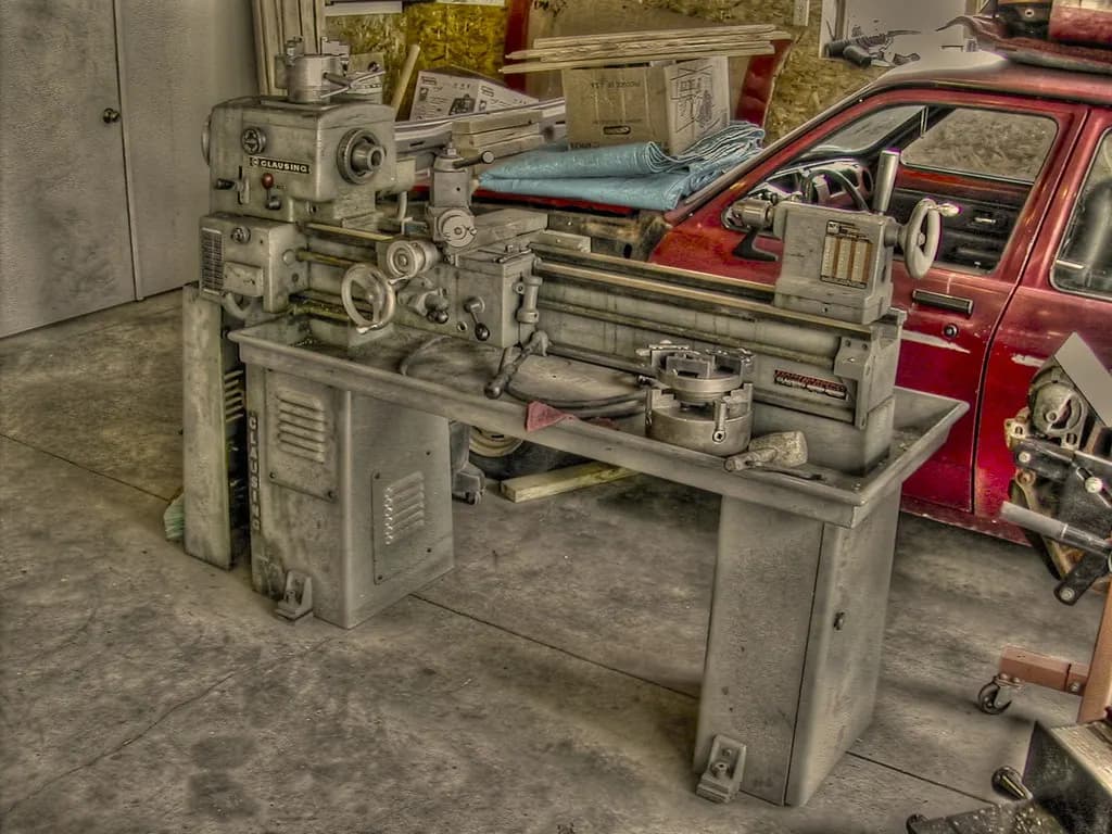 A metalworking lathe on a workshop floor, showing the bed, carriage and chuck