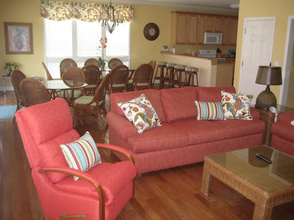 Open-plan living and dining area of a beach house rental with red sofas, wicker dining chairs and a kitchen