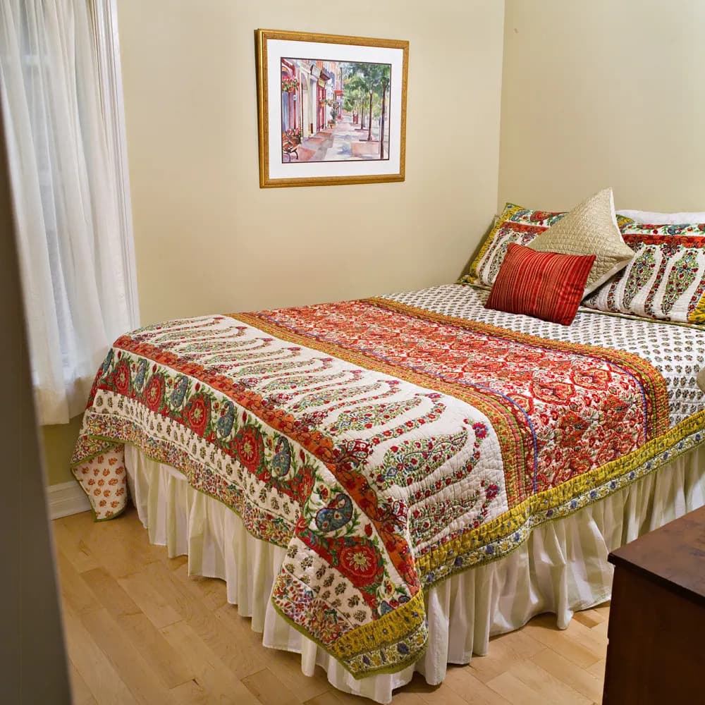 A made-up king bed with a patterned quilt in a bright condo bedroom prepared for guests