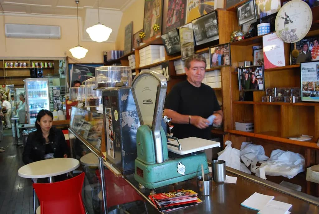 Owner of a small cake shop standing behind the counter with old scales and a cash register
