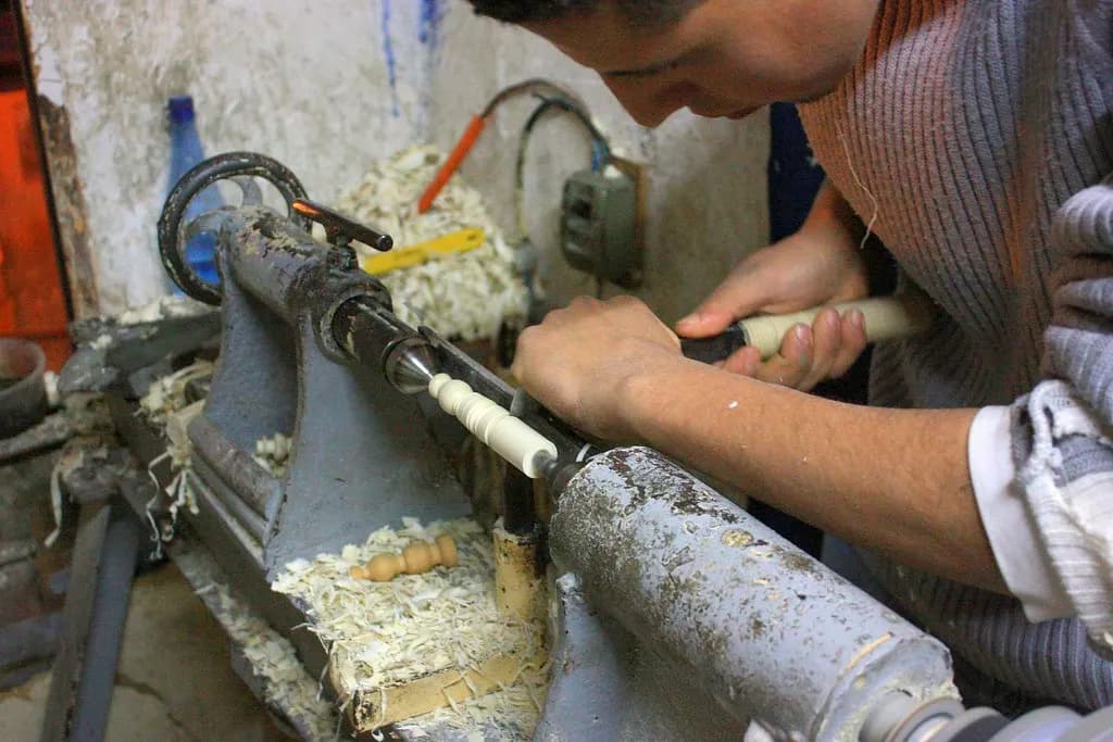 Craftsman turning wooden chess pieces on a lathe in a small workshop