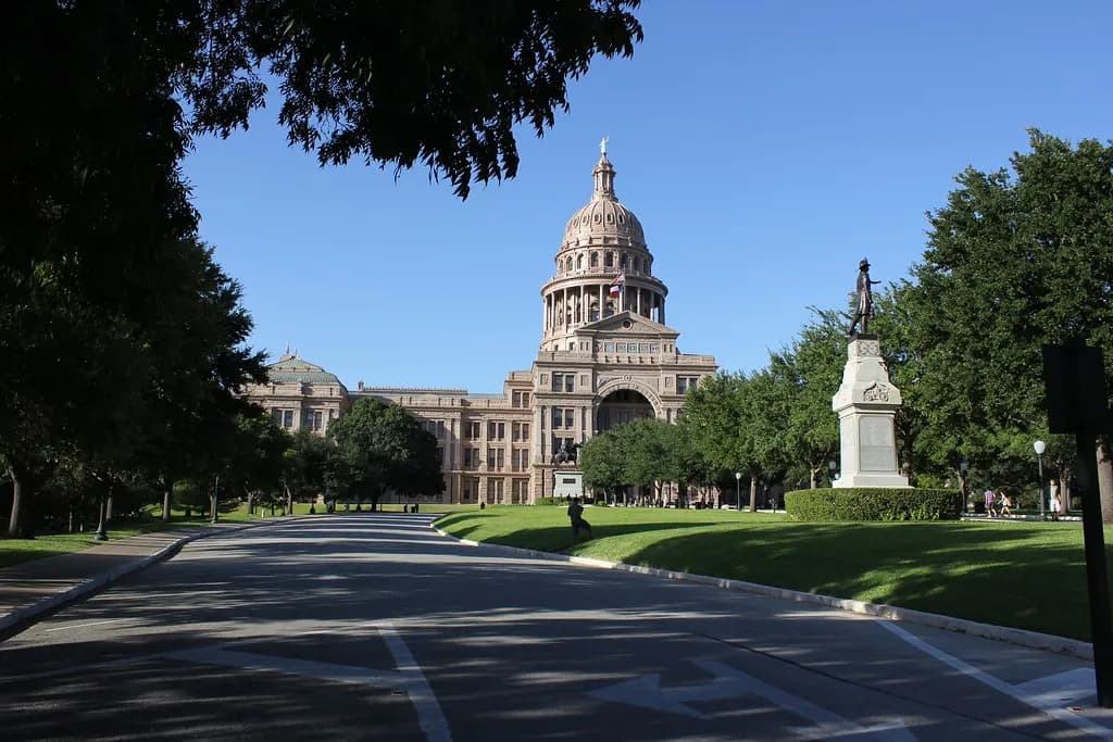 The pink granite Texas State Capitol dome in Austin seen down a tree-lined avenue