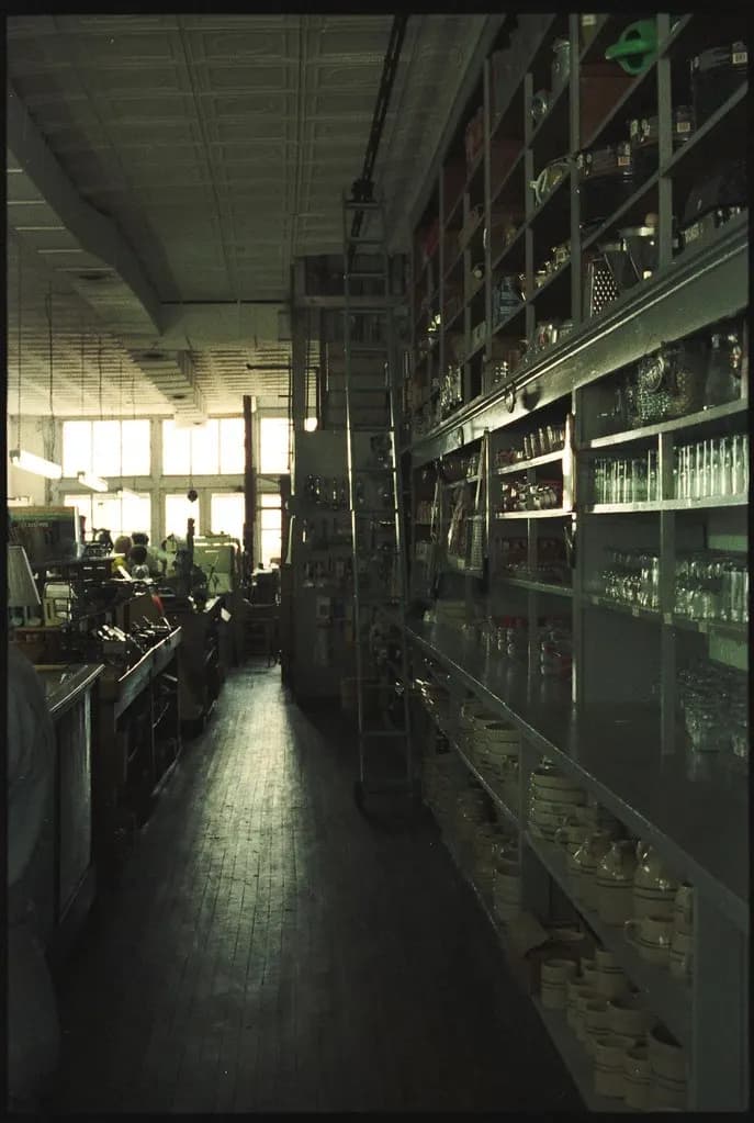 Long aisle of an old independent hardware store with wooden floors and shelves of housewares