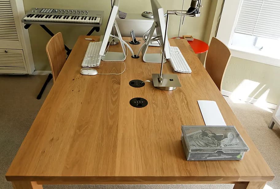 A long wooden office desk with two computer workstations, keyboards and a cable tray