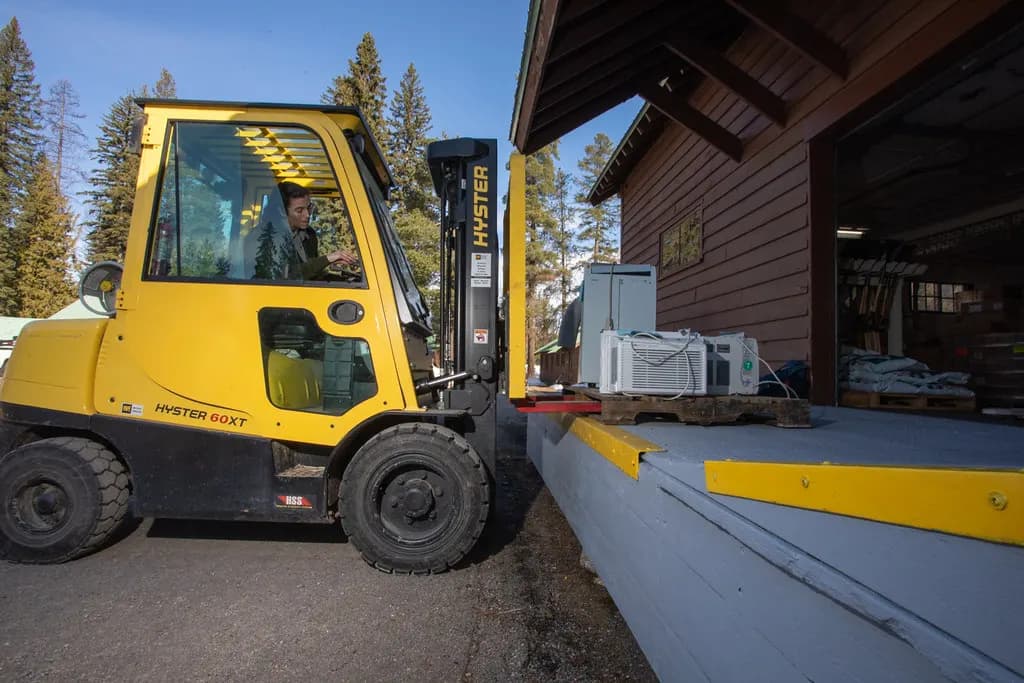 Forklift lifting a pallet of boxed air conditioners onto a wooden loading dock