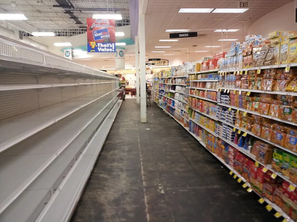 Grocery store aisle with empty shelves on one side and stocked snack shelves on the other