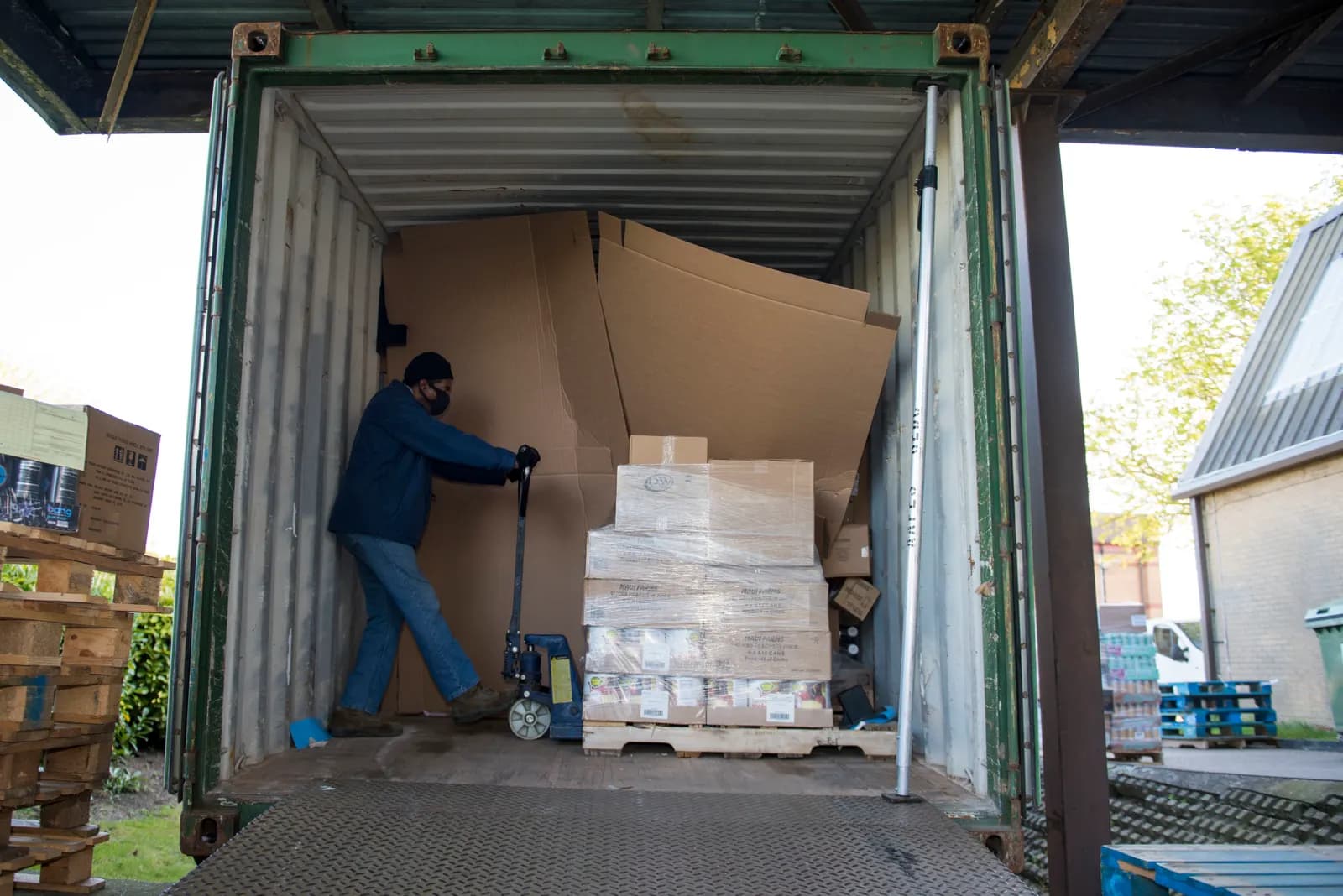 Worker using a pallet jack to unload a pallet of boxed stock from a shipping container