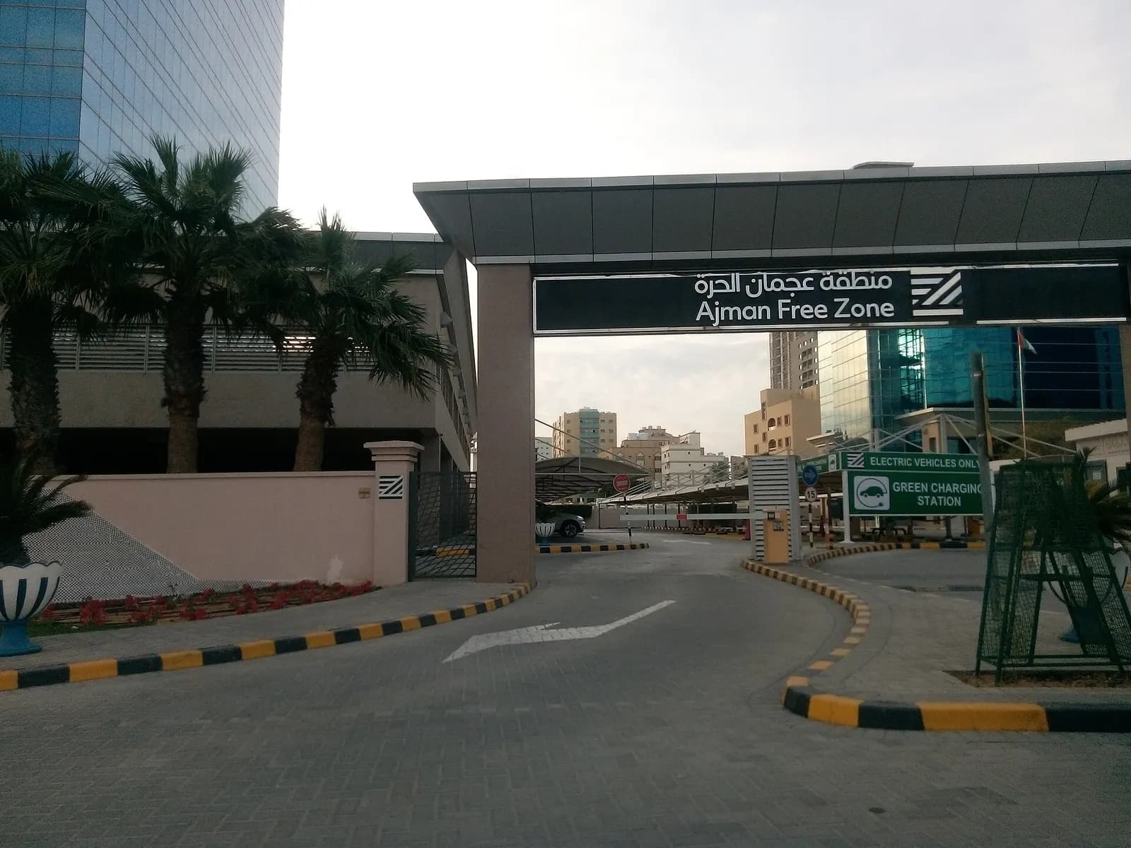 Entrance gate of Ajman Free Zone with its bilingual sign, palm trees and office buildings behind