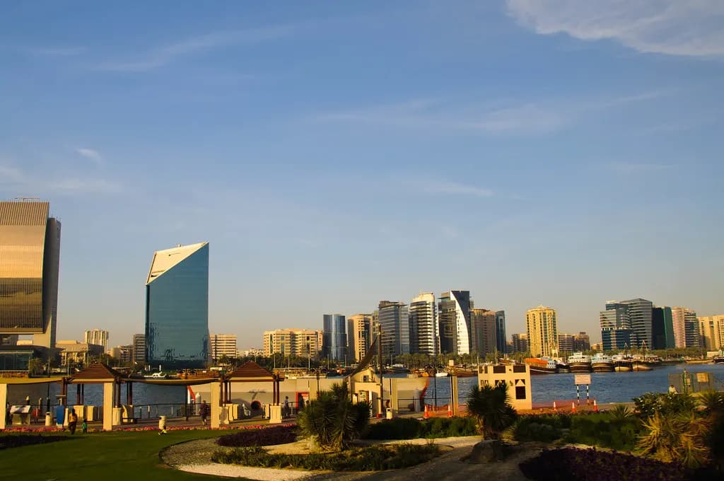 Office towers on the Deira side of Dubai Creek seen from a park in late-afternoon light