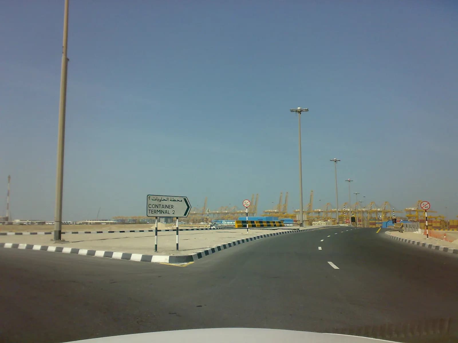 Road inside Jebel Ali Free Zone with a sign pointing to Container Terminal 2 and port cranes in the distance