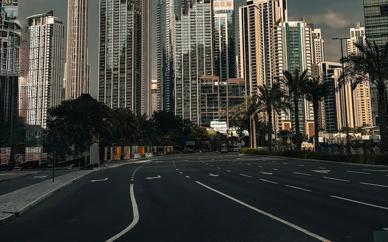 Office towers along a Business Bay road with the Burj Khalifa behind under a cloudy sky